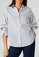 Person wearing a white and Navy striped shirt with rolled-up sleeves on a plain background