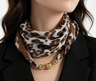 A close-up of a model wearing a leopard print silk scarf with a gold chain link necklace.