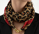 A close-up of a model wearing a leopard print scarf with red side panels and gold metal clasp details, styled with a black blazer.