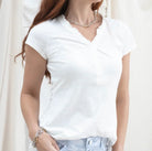Lady wearing a white tee with detail around the neck in front of a white background.