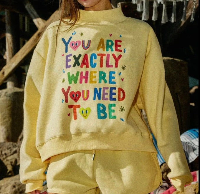 Person wearing a yellow sweatshirt with colorful text in an outdoor setting