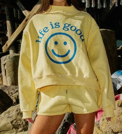 Person wearing a yellow 'Life is Good' sweatshirt with a smiley face graphic.