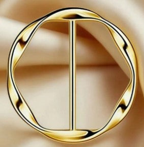A gold-toned metal belt buckle with a twisted circular design and a central vertical bar, shown on a soft beige satin background.