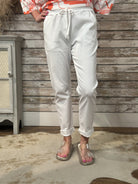 Person wearing white pants and a patterned top in front of a wooden wall.