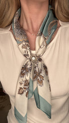 Silky teal and cream pearl magnetic scarf featuring ornate botanical prints with a satin finish and pearl clasp accent.